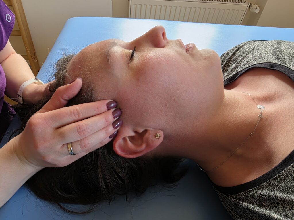 Fizjoterapeuta uciska punkty spustowe w obrębie skroni pacjentki w celu łagodzenia objawów migreny.